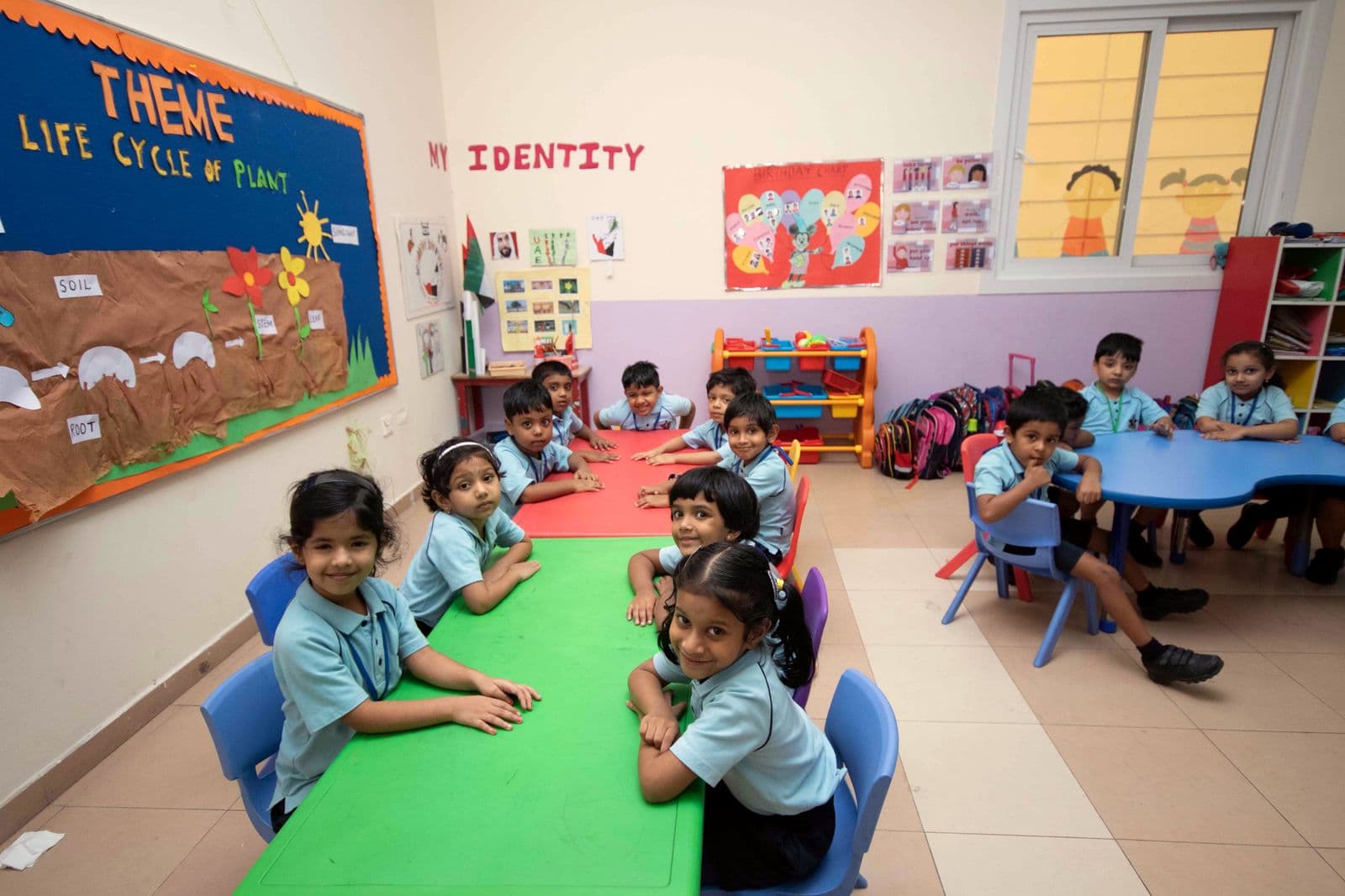 Kindergarten girls smiling at a long green table during a lesson