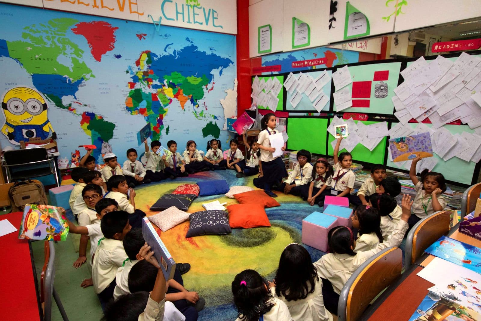 A primary class gathered on colourful cushions in the reading corner