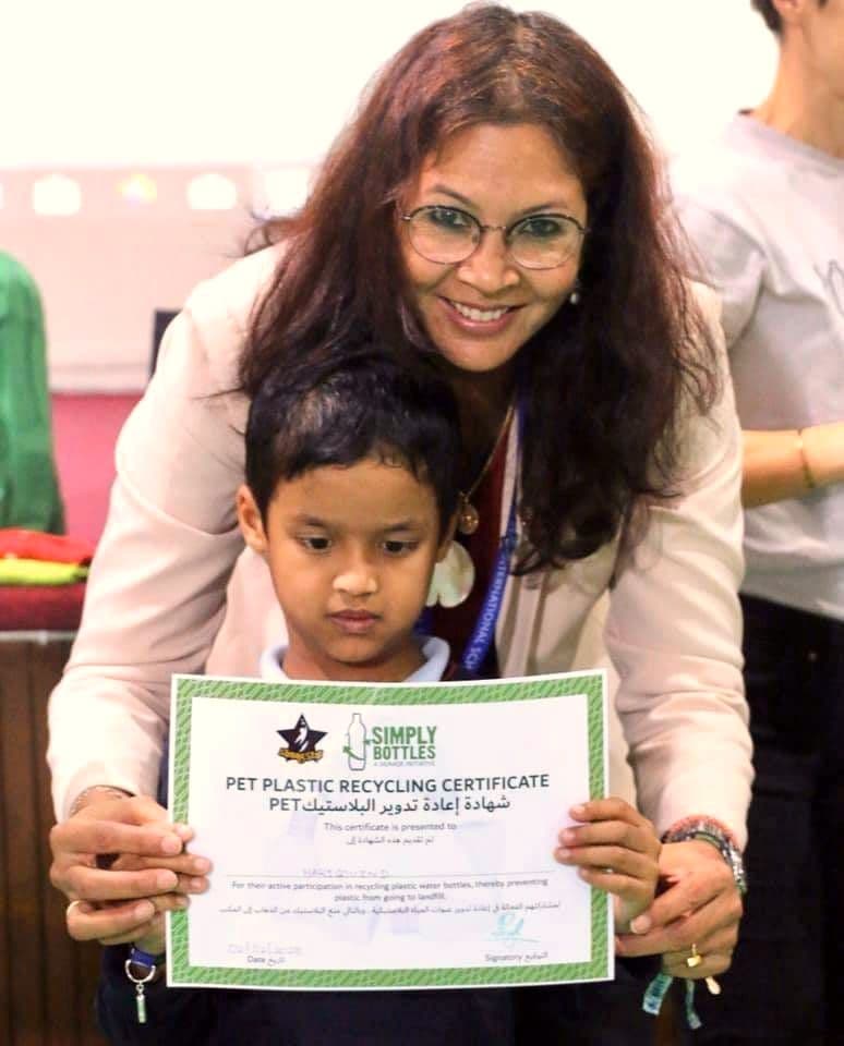 A teacher and a young pupil holding a plastic recycling certificate