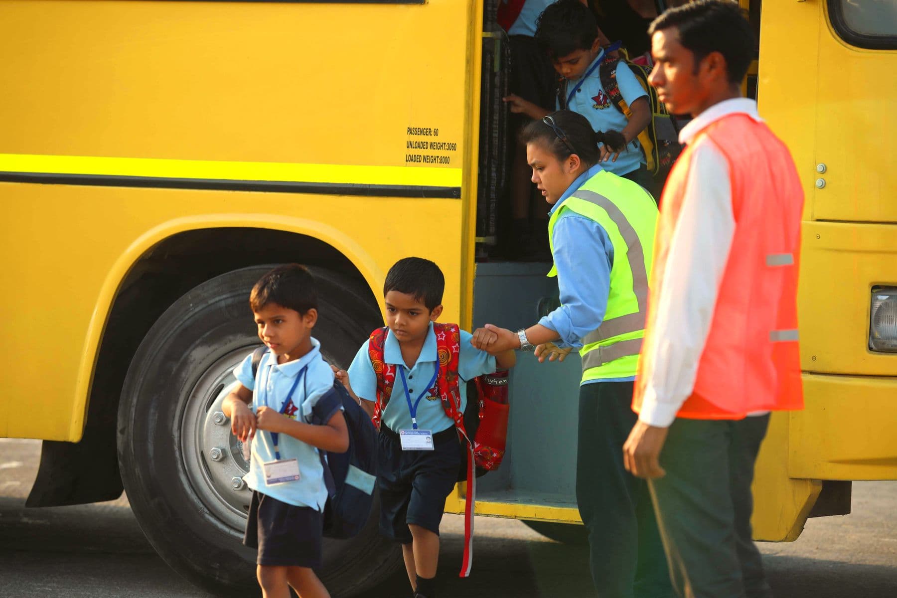 A bus attendant and a supervisor help kindergarten pupils step down from a yellow school bus