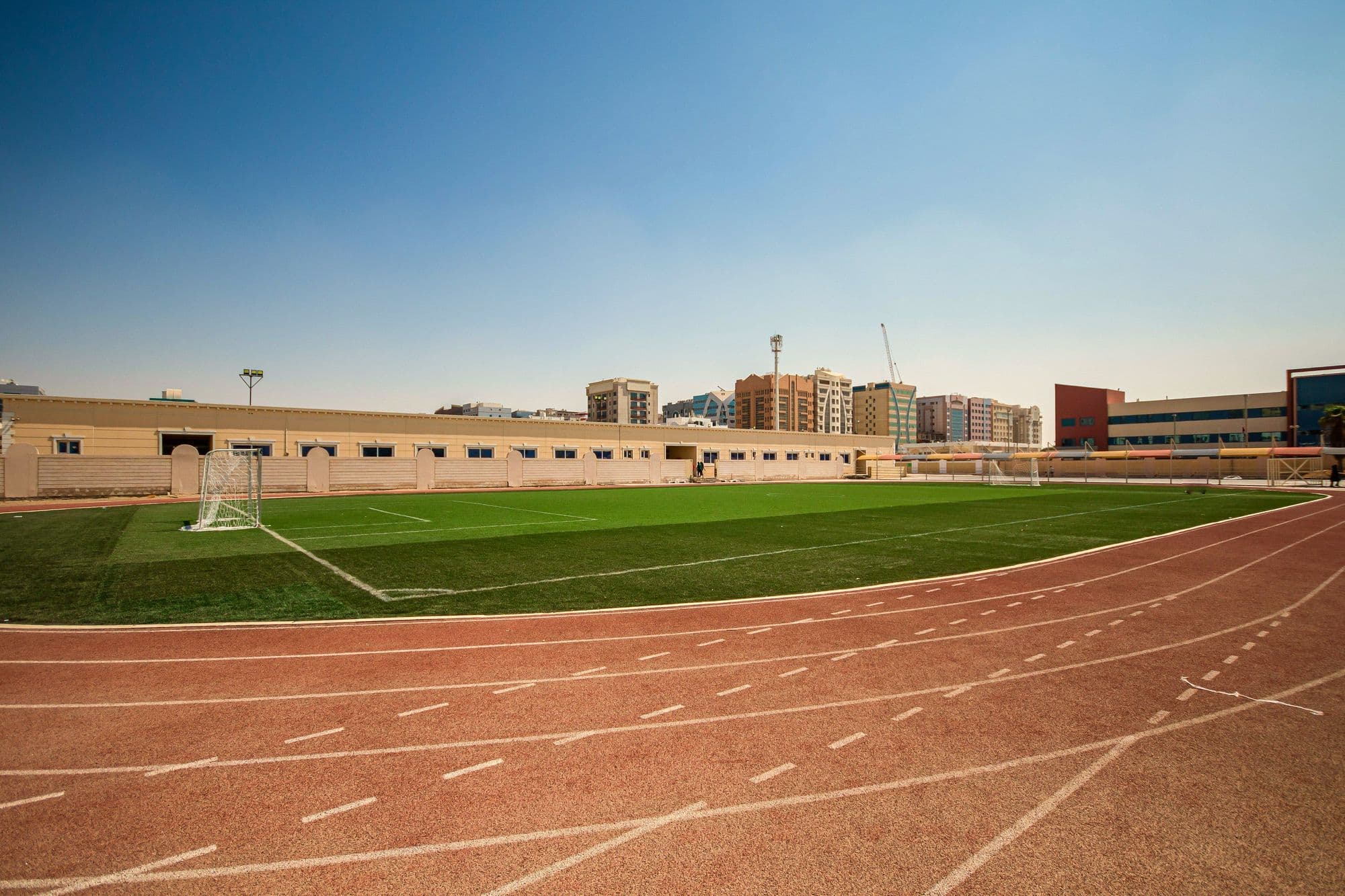 The red running track sweeping around the green football field, with the school buildings beyond